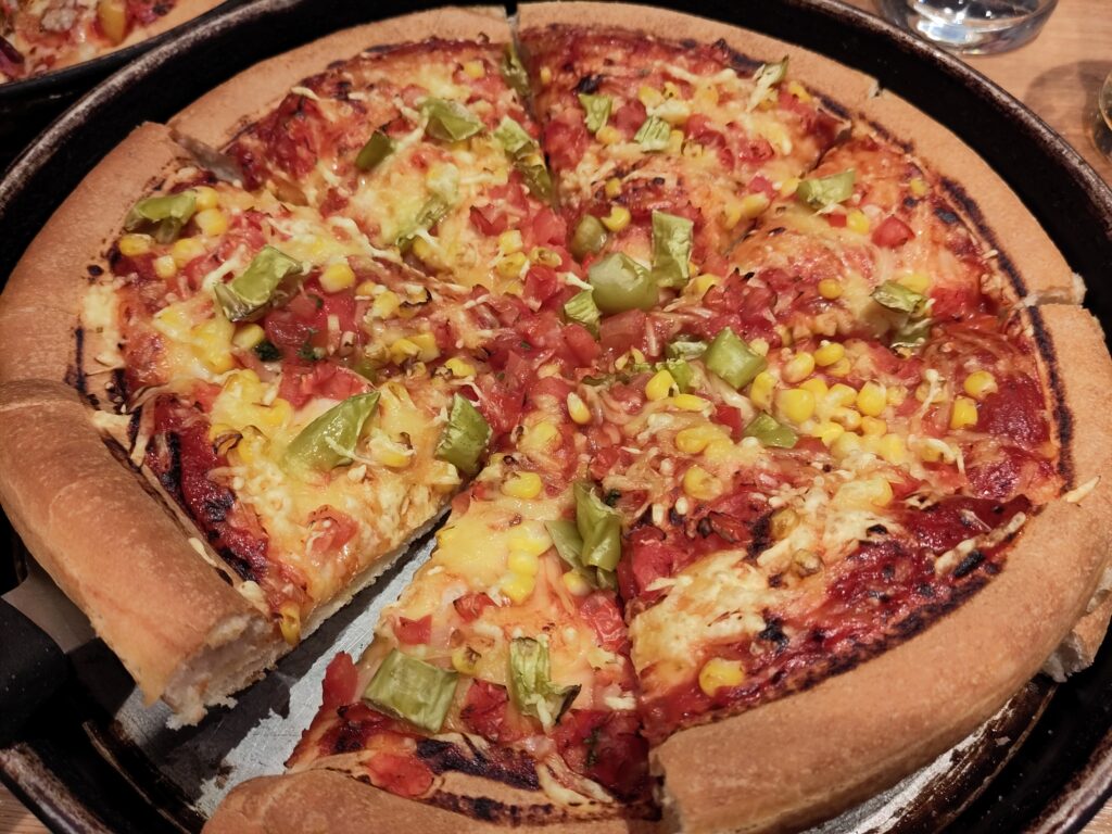 Foto einer Pan-Pizza mit veganem Käse, Pepperoni und Mais.